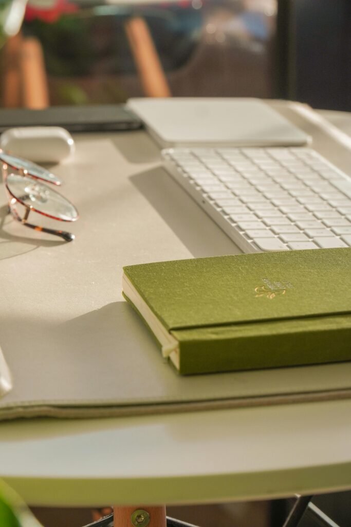 Elegant close-up of a modern workspace featuring a green notebook, eyeglasses, and a keyboard.